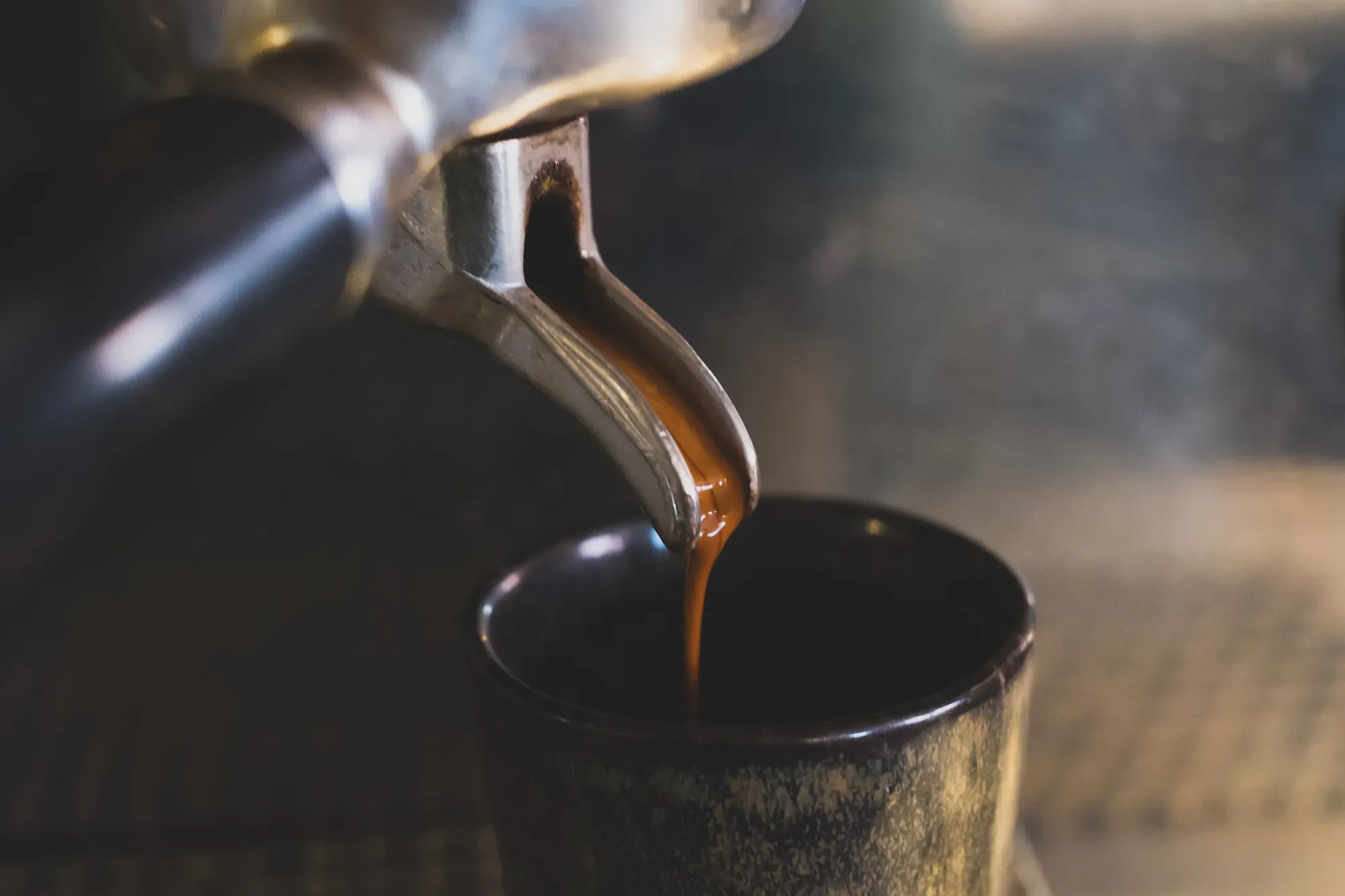 Espresso läuft aus dem Auslauf des Siebträgers in eine dunkle Tasse.