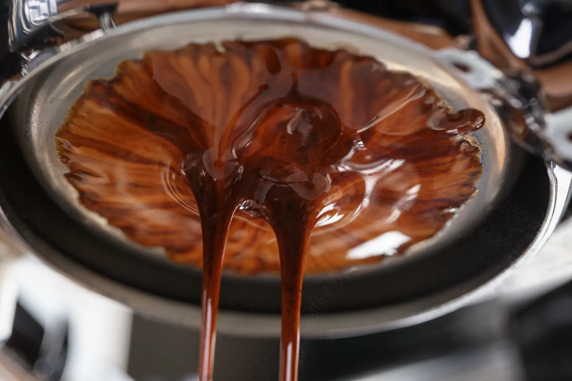 Nahaufnahme eines Siebträgers ohne Boden, aus dem dunkler Espresso mit dichter Crema läuft.