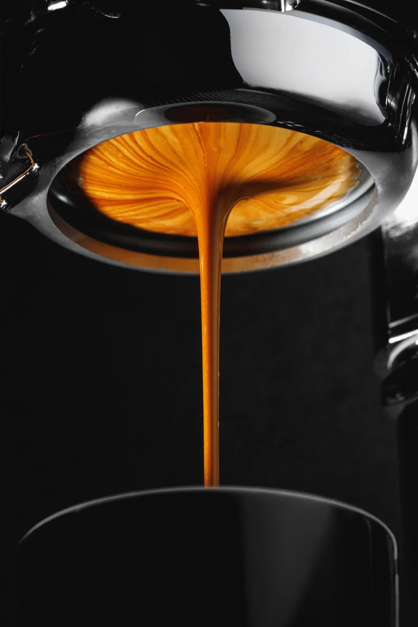 Ein dünner Strahl Espresso läuft aus einem Siebträger ohne Boden in die Tasse.