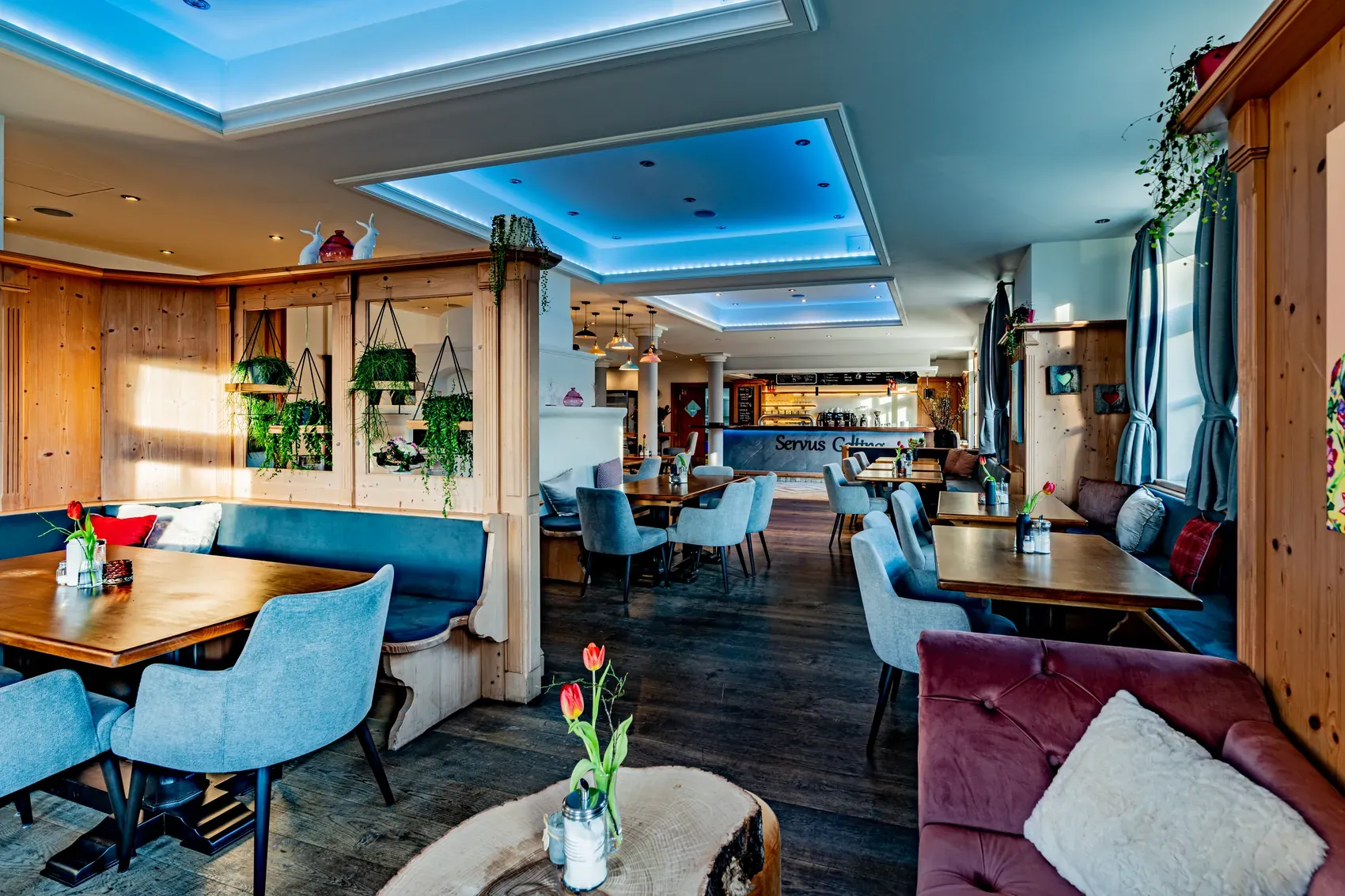 Das Café Servus Gelting von innen: blaue Sessel und Bänke, Holztische und die Theke im Hintergrund.