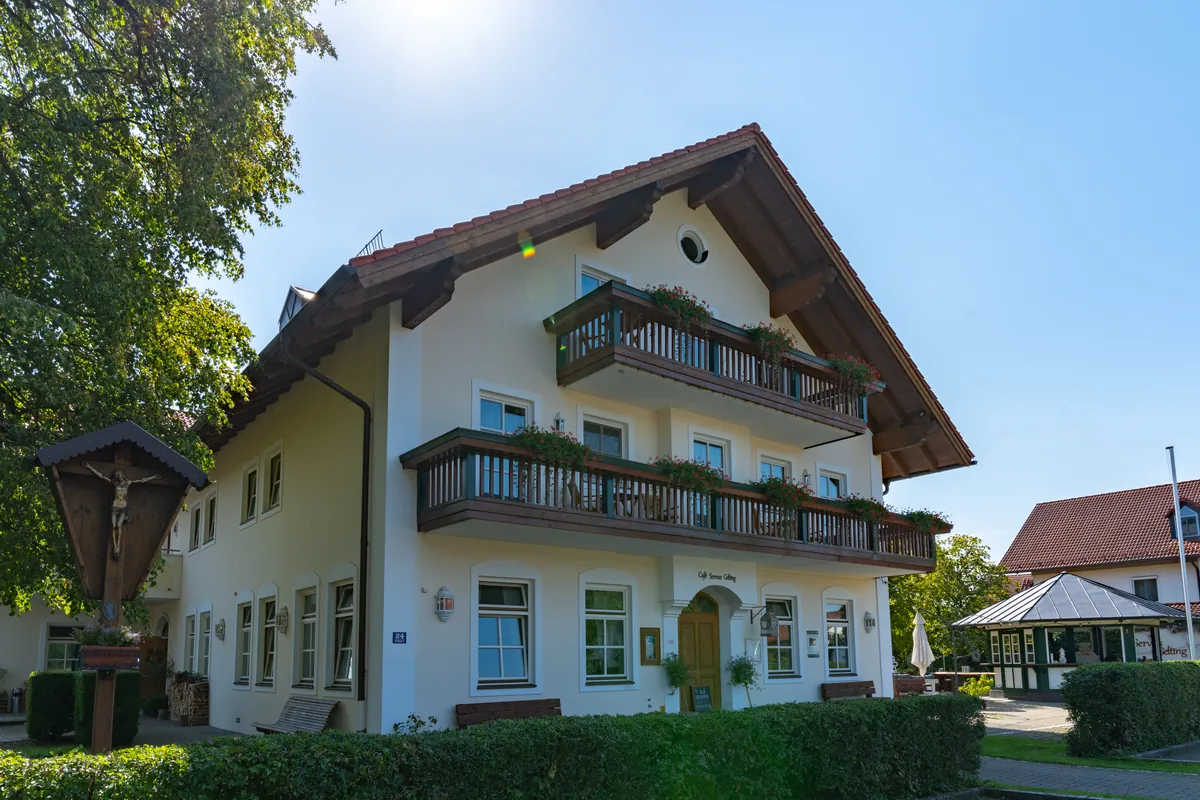 Giebelseite des Hauses Servus Gelting mit Balkonen, Blumenkästen und dem Eingang zum Café.