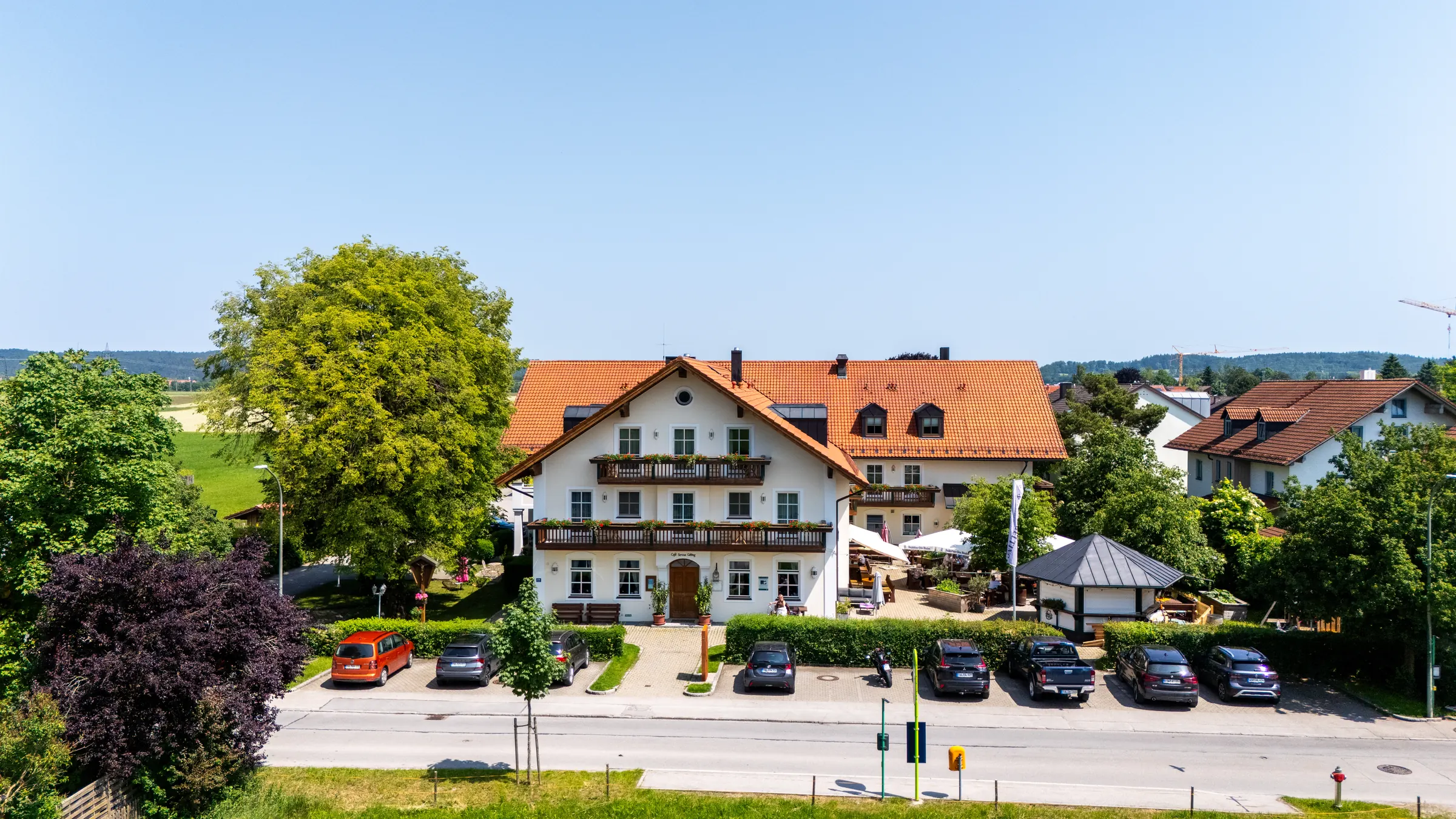 Das Haus Servus Gelting in Geretsried von der Straße aus gesehen, mit rotem Ziegeldach, Balkon und Wiesen dahinter.