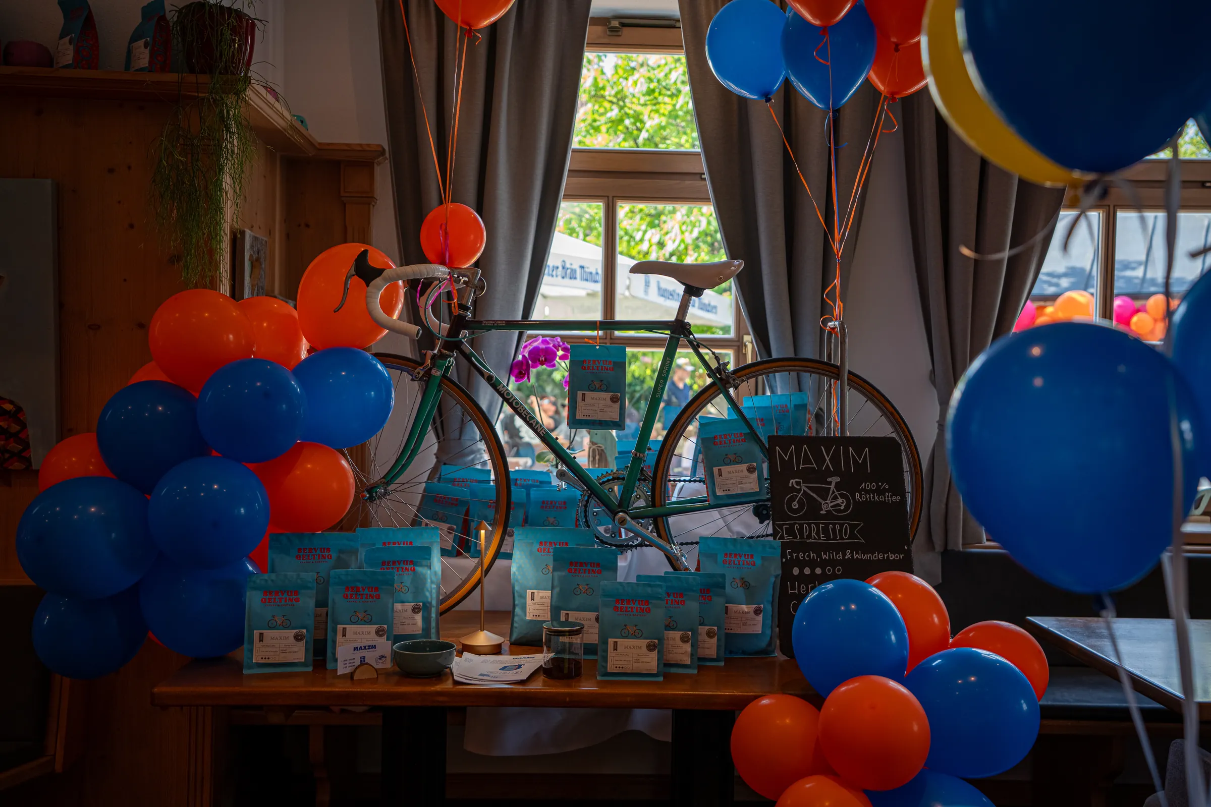 Maxims grünes Rennrad beim Rösterei Opening, davor türkise Kaffeepackungen, rundherum blaue und orange Luftballons.