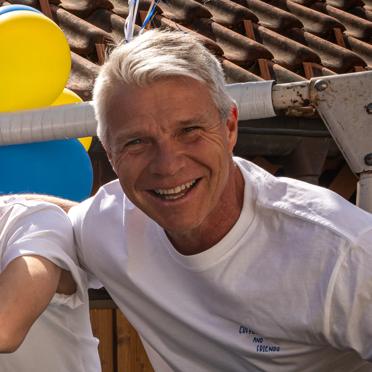 Florian, Röstmeister von Servus Gelting, lacht in die Kamera, hinter ihm gelbe und blaue Luftballons.
